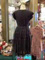 Black dress with red patterns on a mannequin in a store setting.