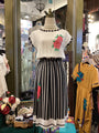 Mannequin wearing a white top with floral embroidery and black striped skirt in a store setting.