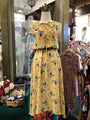Yellow floral dress on a mannequin in a store setting with racks of clothes and decor.