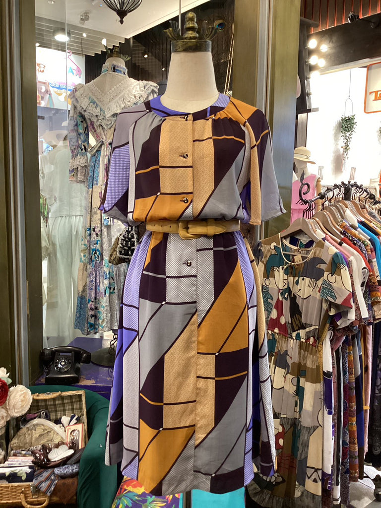 Mannequin wearing a patterned outfit in a store setting with racks of clothes in the background.