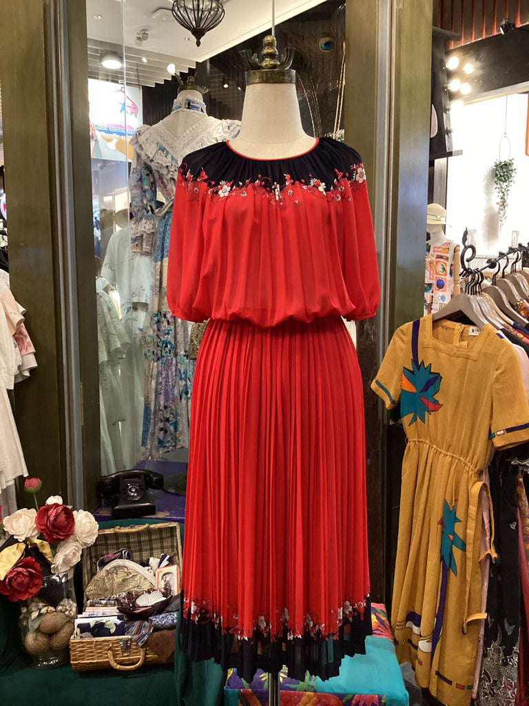 Red dress with black trim on a mannequin in a store setting with other clothing items.