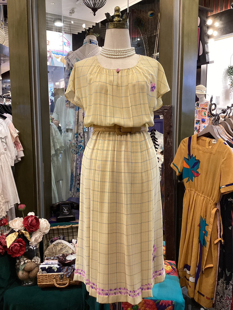 Mannequin wearing a yellow plaid dress in a store setting with other clothing and decor.