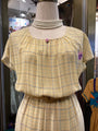 Mannequin wearing a yellow plaid dress with a pearl necklace in a store setting.