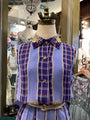 Mannequin wearing a blue and purple plaid dress with gold accents in a store setting.