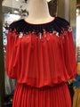 Red dress with black floral embroidery on a mannequin in a store setting.