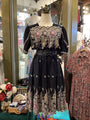 Black dress with intricate floral embroidery on a mannequin in a store setting.
