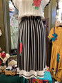 Mannequin wearing a white blouse with floral embroidery and black and white striped skirt in a store setting.