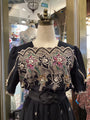 Black dress with intricate lace detailing on a mannequin in a store setting.