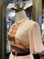 Mannequin wearing a patterned dress with a colorful top and white skirt in a store window.