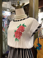 Mannequin wearing a white top with red floral embroidery in a store setting.