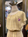 Mannequin wearing a yellow plaid dress with floral embroidery in a store setting.