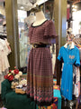 Mannequin wearing a patterned dress in a store setting with other clothing and decor.