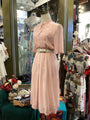 Vintage-style pink dress on a mannequin in a store setting with other clothing items.