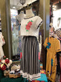 Mannequin wearing a white top with floral embroidery and black and white striped skirt in a store setting.