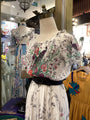 Floral dress on a mannequin in a store setting with other clothing items.