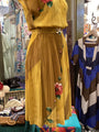 Mannequin wearing a yellow pleated dress with floral embroidery in a store setting.