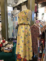 Yellow floral dress on a mannequin in a clothing store with various dresses and accessories.