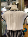 Mannequin wearing a white blouse with black trim and a pearl necklace in a store setting.
