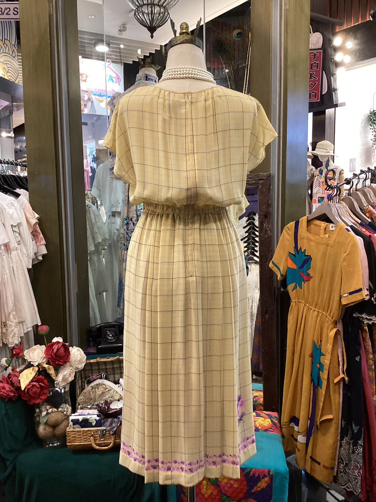 Mannequin wearing a yellow plaid dress in a store setting with other clothing items.