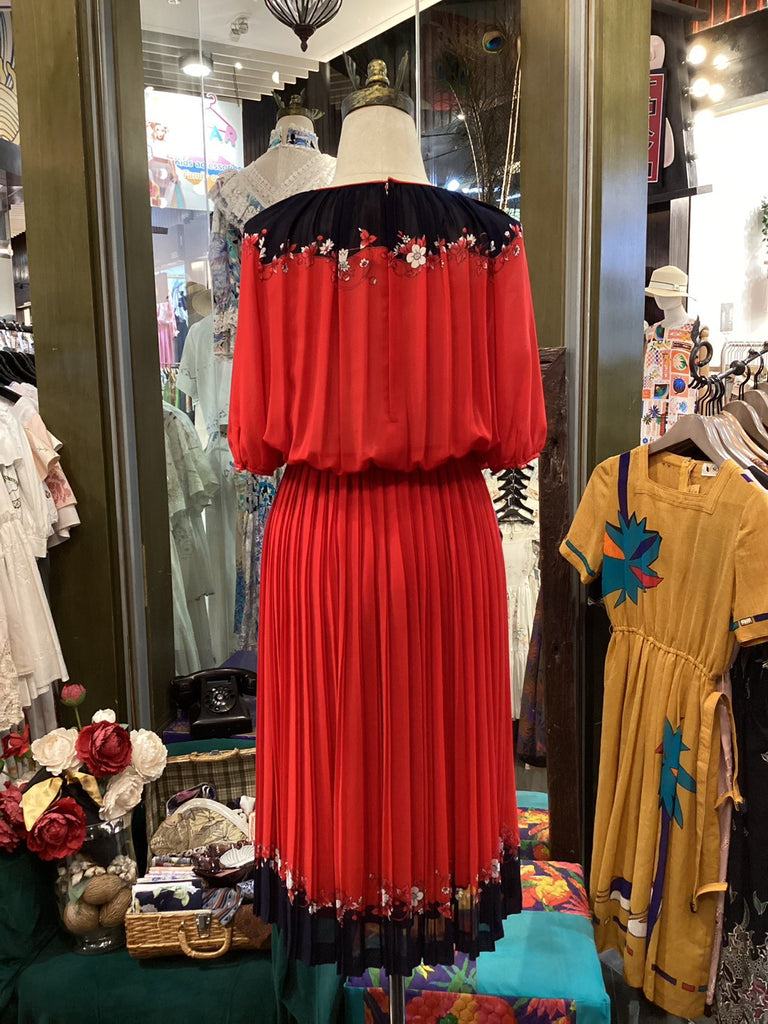 Red dress with black trim on a mannequin in a store setting with other clothing items.