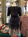 Black dress with intricate embroidery on a mannequin in a store setting.