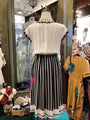 Mannequin wearing a white top and black and white striped skirt in a store setting with other clothing items.