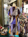 Mannequin wearing a colorful geometric-patterned dress in a store setting with other clothing items.