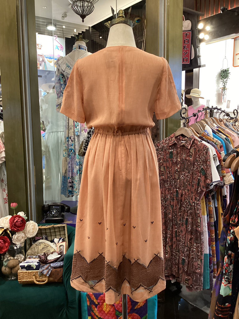 Vintage peach dress on a mannequin in a store setting with other clothing items.