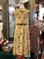 Mannequin wearing a yellow floral dress in a store setting with other clothing items.