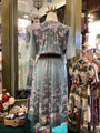 Mannequin wearing a floral dress in a store setting with racks of clothes in the background.